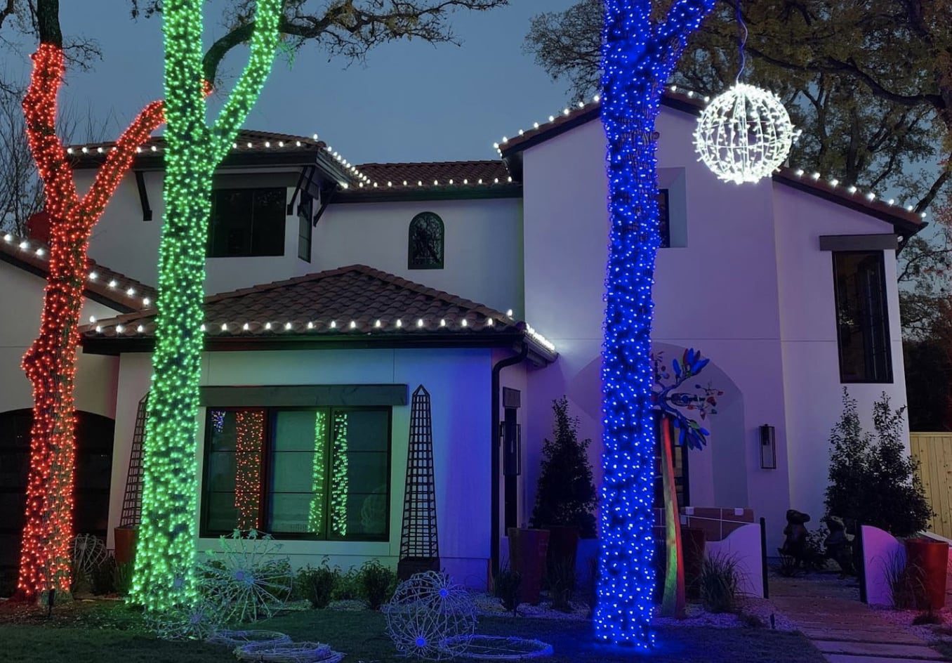 House with colorful lights wrapped around trees